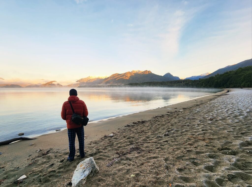 Trekker watching sunrise over Lake Manapouri from the beach near Moturau Hut on the Kepler Track