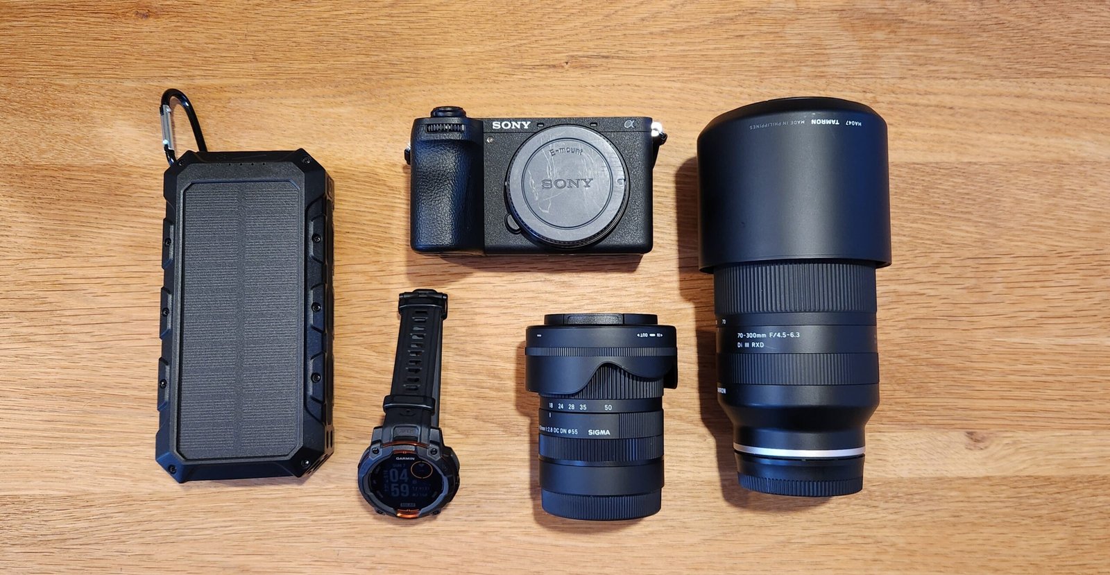 Tech for the EBC trek flat-lay — solar power bank, Garmin Instinct 3 Solar, Sony A6700 mirrorless camera, Sigma 18-50mm and Tamron 70-300mm lenses